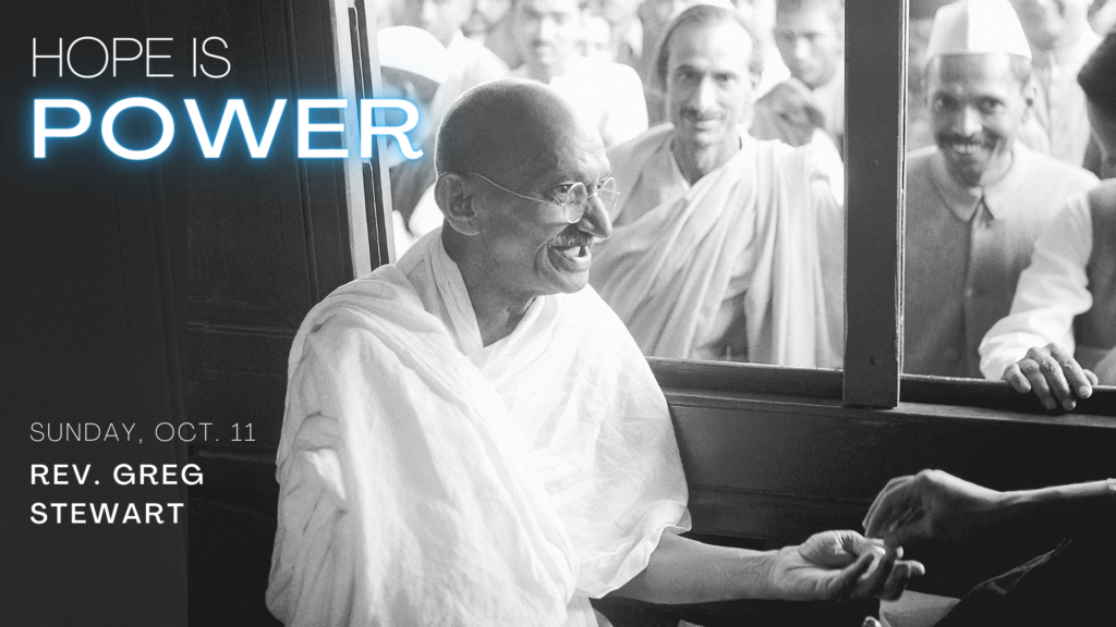 Black and white photo of Mahatma Gandhi on a train with people looking in